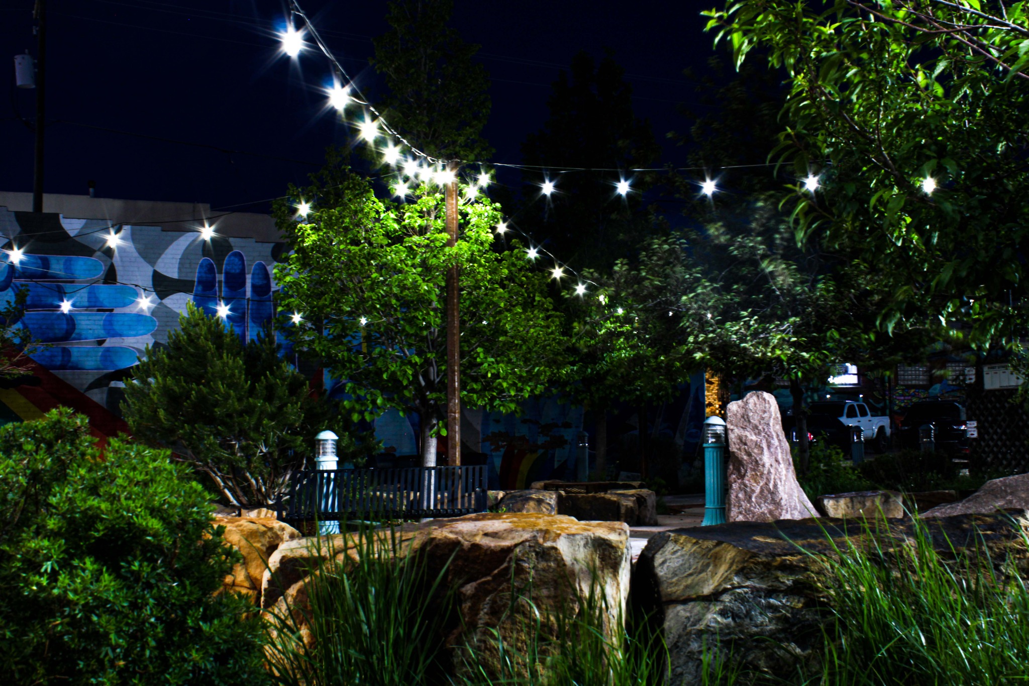 Plaza at night — string lights and mural.